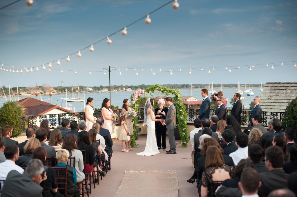 A rooftop wedding ceremony with string lights and a floral arch overlooking a harbor, a unique Florida wedding venue example. 