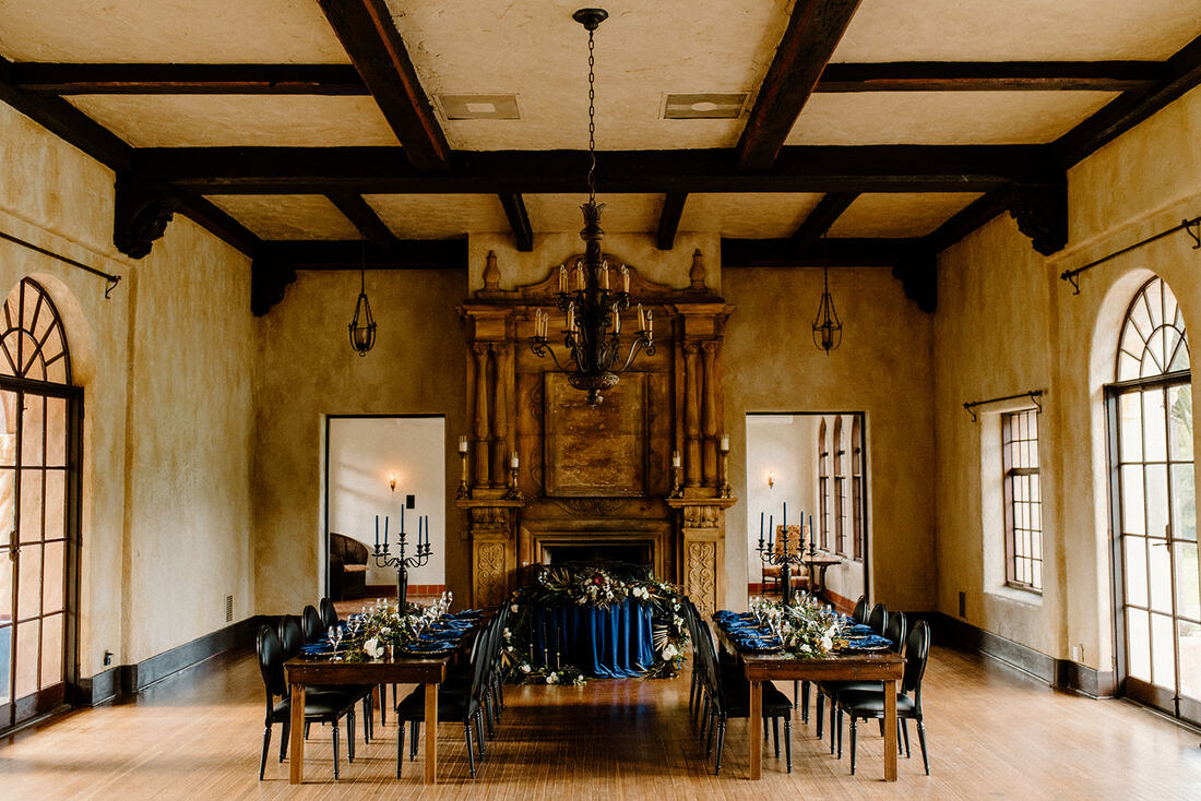 Interior of the historic Lightner Museum set for a wedding reception with a large fireplace and dark wood beams.